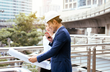 Male and female industrial engineers using two-way radio communication and holding blueprints while...