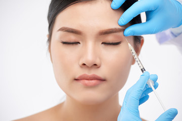 Young Asian woman getting rejuvenating botox injection under brow