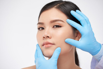Gloved hands of cosmetologist examining flawless face of beautiful young woman