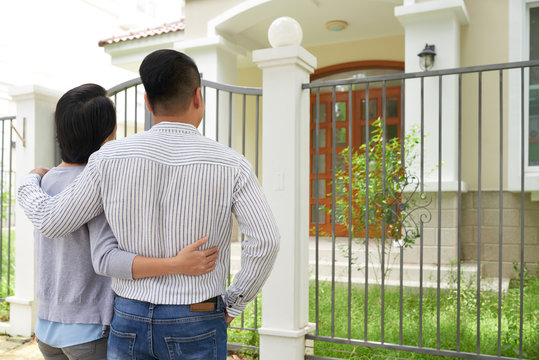 Rear View Of Young Couple Looking At Big House They Want To Buy