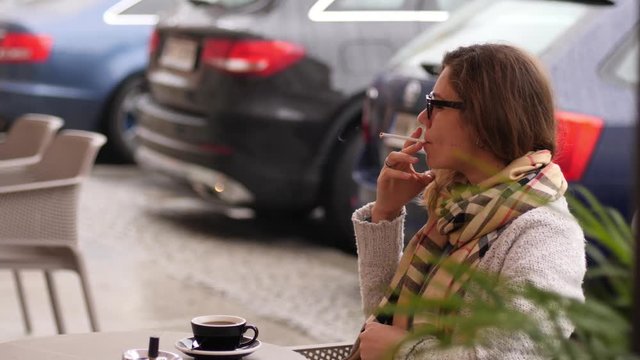 Woman sit smoking cigarette at the street cafe table while drinking coffee