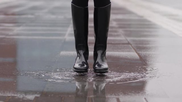Good mood for rainy weather woman in rubber boots with high bootleg jump in puddle with splash