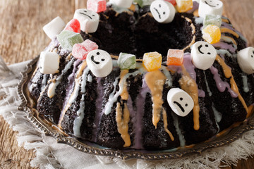 Halloween dessert: dark Bundt cake with candied fruits, marshmelow and colorful glaze close-up. horizontal