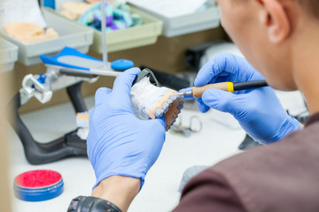 A dental technician dentist working with prostheses in a laboratory with wax on a jaw model