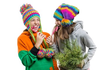 Young cheerful teenage girls having fun with Christmas candy canes, in winter knitted caps, isolated on white background