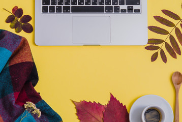 Laptop with coffee, herbarium and blanket on yellow background. Autumn. Flat lay. Top view. Copy space