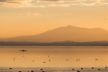Beautiful view of a lake at sunset, with orange tones, birds on water and a man on a canoe
