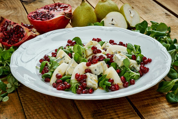 delicious salad of pear gorgonzola cheese and lettuce on a white plate on a wooden table