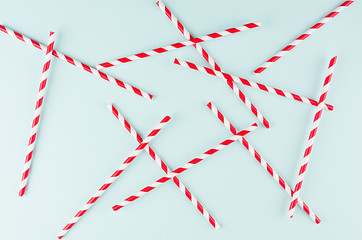 Red striped cocktail straws on pastel mint color as abstract joyful background, random pattern.