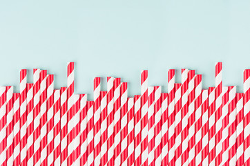 Red striped cocktail straws on pastel mint color as abstract joyful background, border with copy space.