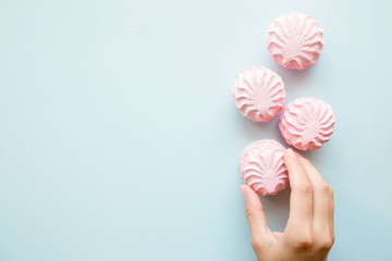 Woman's hand taking a fluffy, airy, pink zephyr. Mockup for different ideas. Empty place for positive text, quote or sayings on pastel blue table.