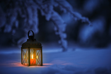Candle lantern under the snowy branches at dusk. Christmas time in a wintery garden.