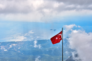 View from the Peak of Tahtali Mountain or Olympus to Kemer and the Gulf of the Mediterranean Sea, against the background of the flag of Turkey, the clouds and the blue sky