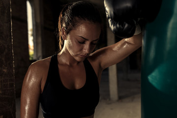 Female boxer resting after punching a boxing bag in warehouse.