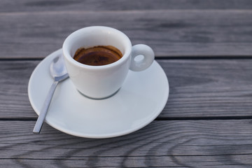a cup of black coffee on a saucer with a small spoon close-up