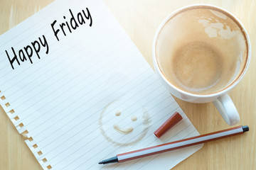 Concept Happy firday message on notebook, pencil and coffee cup on wooden table.