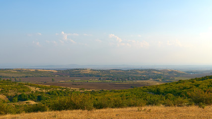 Obraz premium The top view on the valley among the Old Balkan Mountains. In the background, Burgas Lake and an oil refinery. Bulgaria.