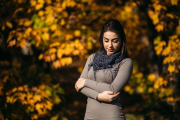 Beautiful happy smiling girl wearing long dress and autumn scarf standing in forest surrounded by yellow trees