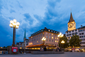 Fototapeta na wymiar Beautiful cityscape of Zurich, Switzerland, with the St. Peter and Fraumunster churches and people relaxing at the bridge over the river Limmat in the blue hour in summer on July 25, 2014 