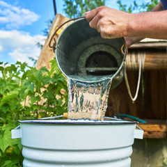 Man pouring water just taken up from a well into a enameled bucket