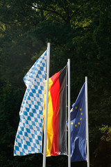 Drei im Wind flatternde Flaggen. Bayerische Flagge, Deutschlandflagge und Europaflagge 