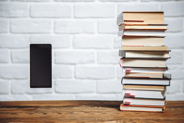 Modern smartphone with blank screen and pile of books on a desk. Technology vs traditional learning education abstract concept.