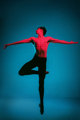 The male athletic ballet dancer performing dance on dark blue background. Studio shot. Ballet concept. Fit young man. Caucasian model