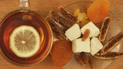 Glass cup with hot tea and saucer with tahini halva and dried fruits on the wooden board 