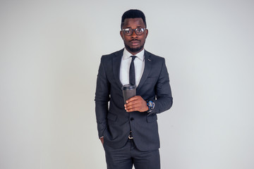 Handsome young African man in formal black suit holds a plastic paper cup with hot coffee cocoa (tea) to go . businessman on coffee break after meeting on white background in studio