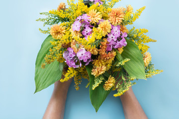 Autumn bouquet of yellow wildflowers in female hand on blue.