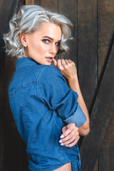 Fototapeta premium attractive young woman in denim shirt standing in front of rustic wooden door and looking at camera