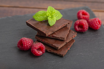 Chocolate with pieces of dry raspberries and fresh raspberries with a mint leaf on a slate plate. Close up.