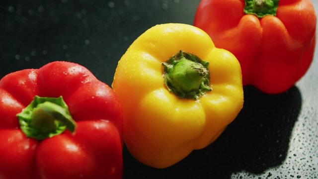 From above view of fresh red and yellow peppers with green stems placed in line on black background covered with drops