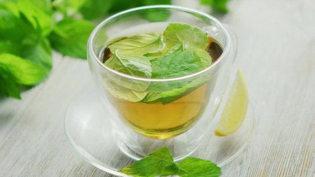 From above view of glass cup of green tea with leaves of mint and slice of lemon placed on saucer on wooden background