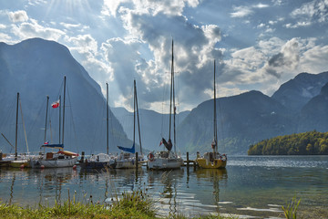 HDR landscape view of mountains with dramatic cloudy sky with anchoring yachts on the lake near Hallstatt village in Austria.