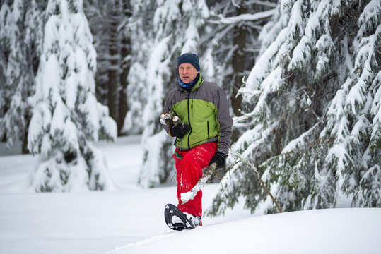Adventurer with firewood in his hands is walking in snowshoes