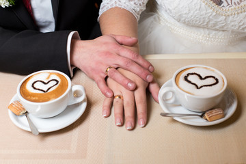 Wedding couple at cafe. Wedding couple holding hands sitting at wooden table with warm coffee in cups in cafe.