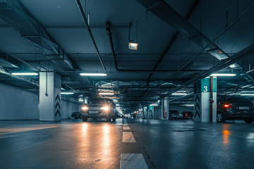Large hall with columns of underground car parking garage with many automobiles in modern mall or...