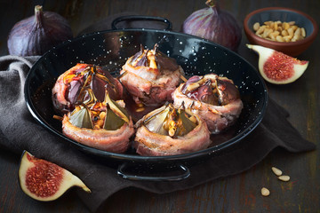 Baked figs wrapped in slices of bacon with pine seeds and honey on dark