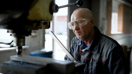 Close-up shot of an old, professional plant worker working at the standing drill machine oil up.