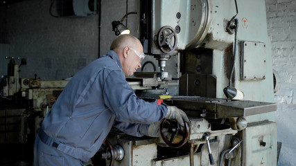 An elderly man in production. A worker on a machine drills a metal part.