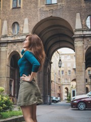Fototapeta na wymiar Brunette girl in a skirt and with long hair, standing, posing in the courtyard of a historic building in St. Petersburg, the entrance of the house, the house is made of numerous huge arches