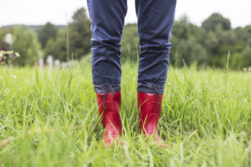 Legs in red rubber boots stand on wet grass