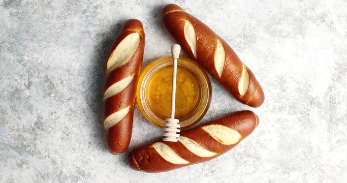 From above view of three fresh baked French loafs with bowl of honey placed in middle on white background of tablecloth