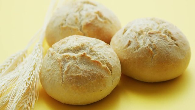 From above view of three round loafs of bread with wheat placed near on yellow background
