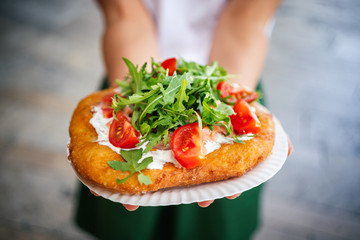 Fototapeta premium A young woman holding a traditional Hungarian Langos with cheese, rucola and tomatoes , Budapest, Hungury