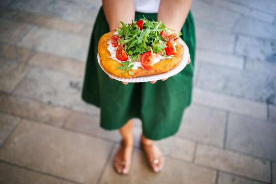 A young woman holding a traditional Hungarian Langos with cheese, rucola and tomatoes , Budapest, Hungury