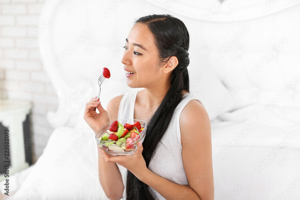 Wall mural Asian woman eating healthy fruit salad at home