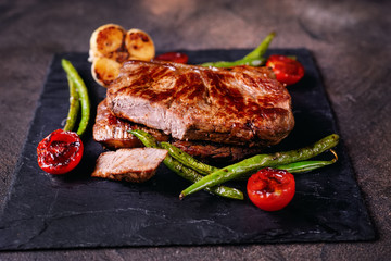 Delicious grilled steaks with vegetables on slate plate