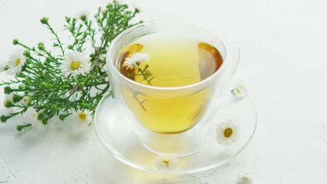 Closeup of glass transparent mug filled with fresh herbal tea with flowers of camomile